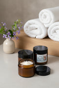 Two small jars with black lids on a light surface with towels and flowers