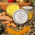 Turmeric body butter with turmeric root and black beads on a leopard print cloth.