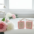 Two small pink soaps with labels on a bath tub with flowers