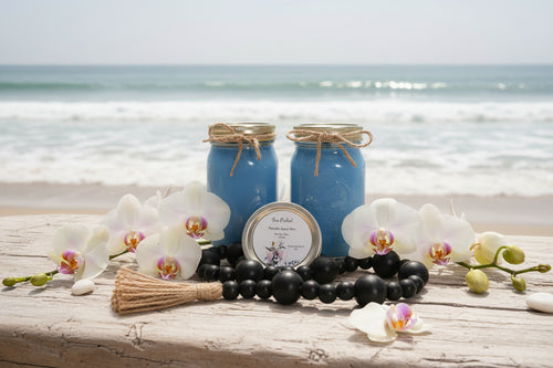 Two blue candles with twine, a broom, and orchids on a wooden surface with a beach background.