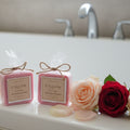 Two small pink bars of soap with labels on a white bath tub with roses