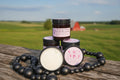 Jars of body butter on a wooden surface with a blurred field background