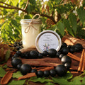 Candle and wax container on a wooden surface with leaves and cinnamon sticks in the background
